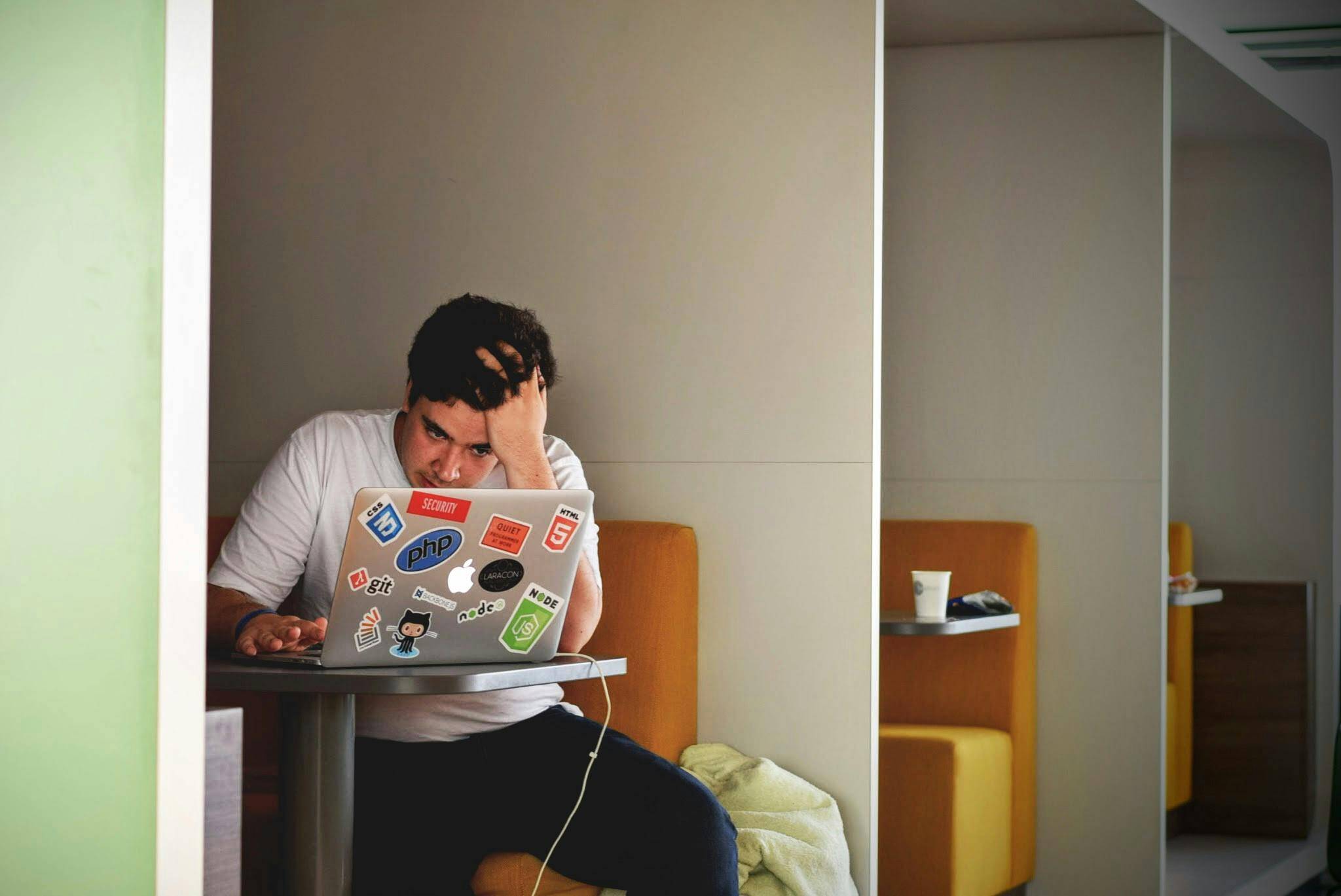 A stressed out worker sitting in a booth with their laptop.