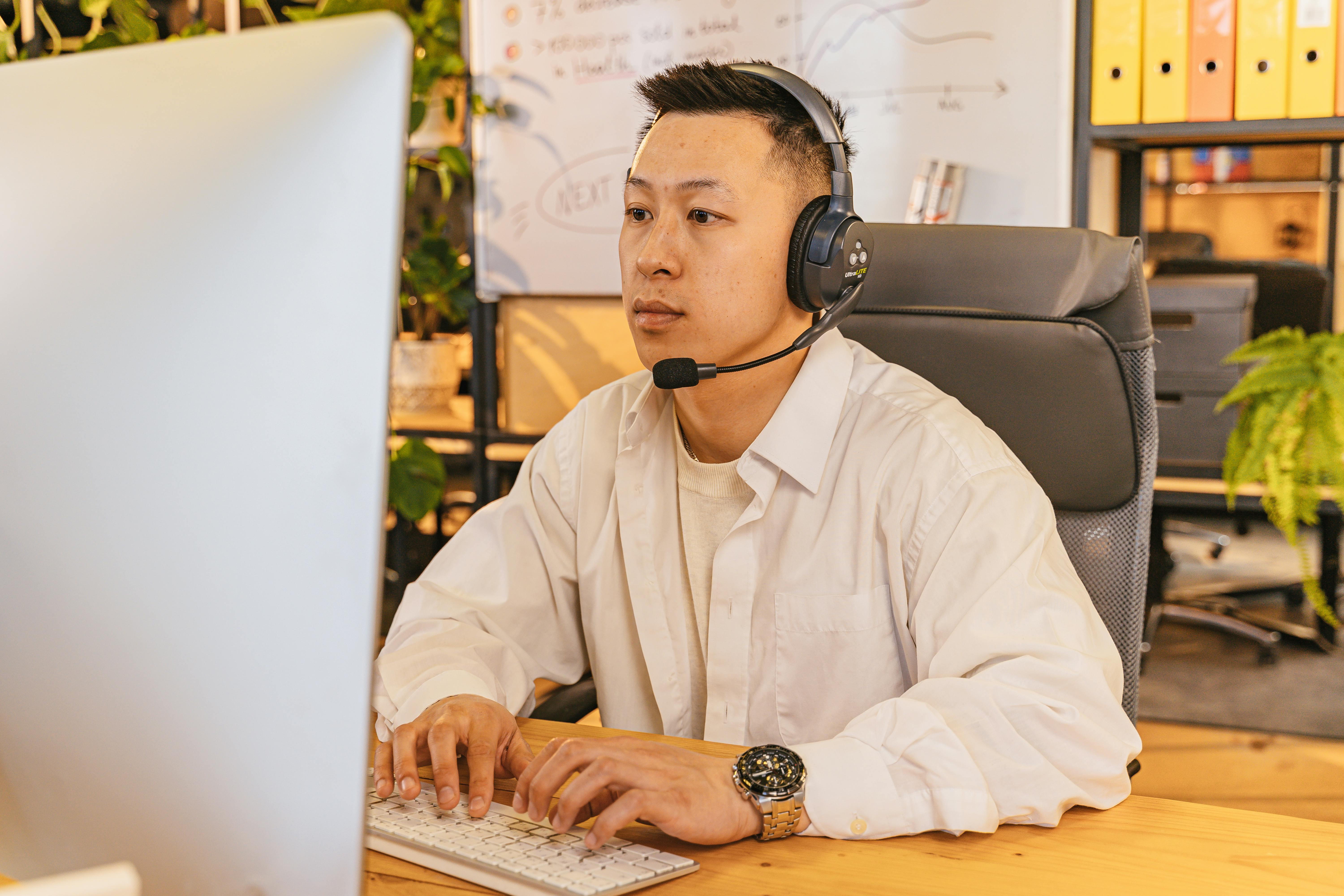 A man in a white shirt, wearing a headset and working on a computer